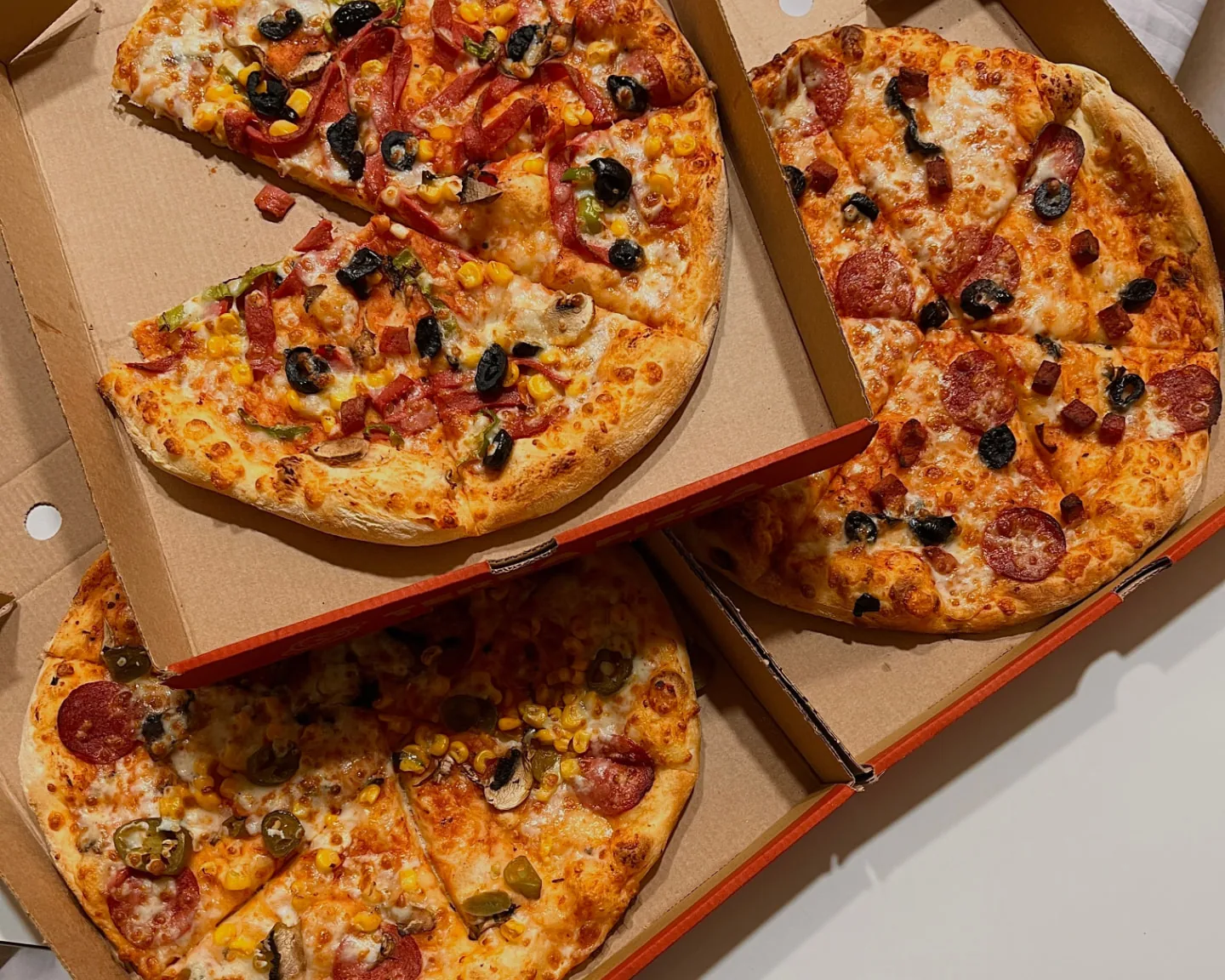 Tre öppna pizzakartonger med hela pizzor på ett ljust underlag.